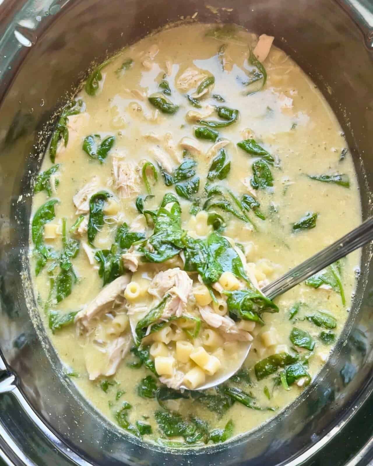 Creamy chicken pesto soup in a slow cooker with fresh spinach and pasta, ready to serve.