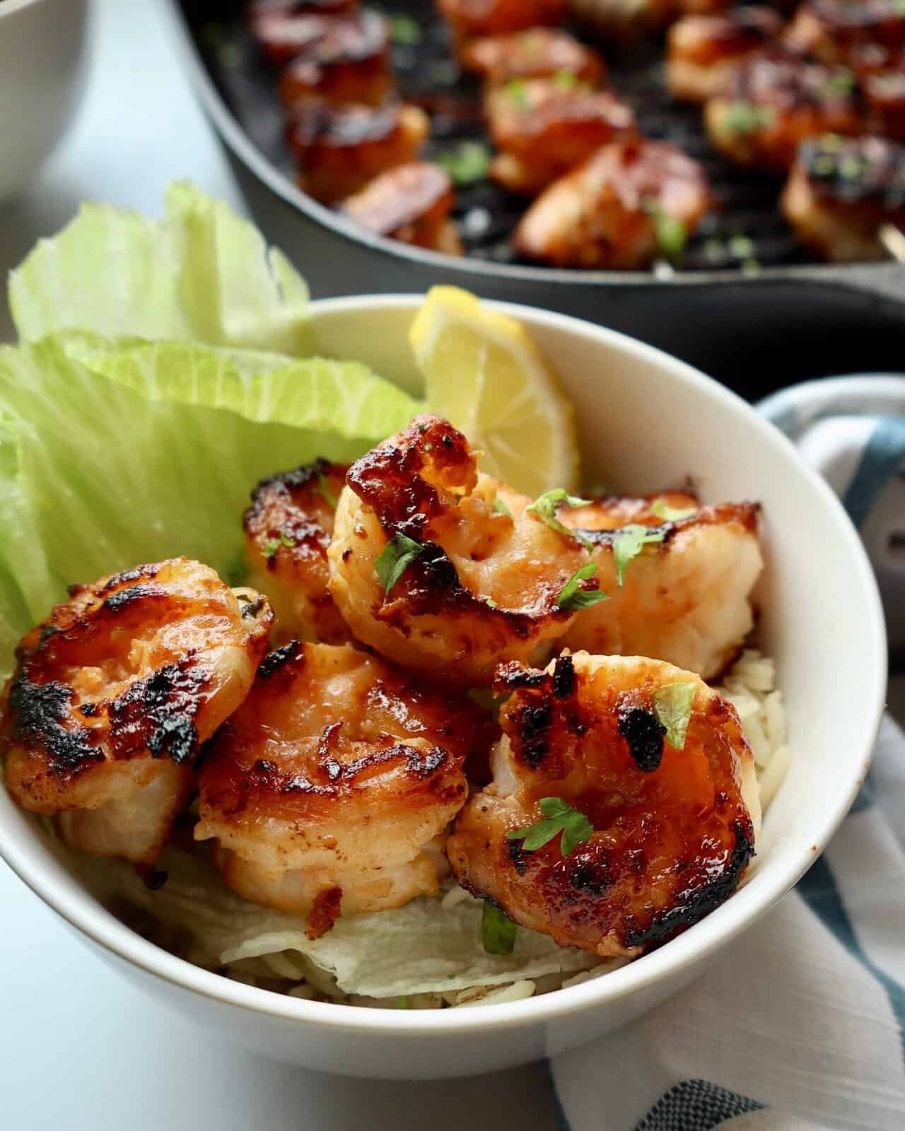 Succulent honey garlic shrimp with fresh lemon and lettuce in a white bowl.