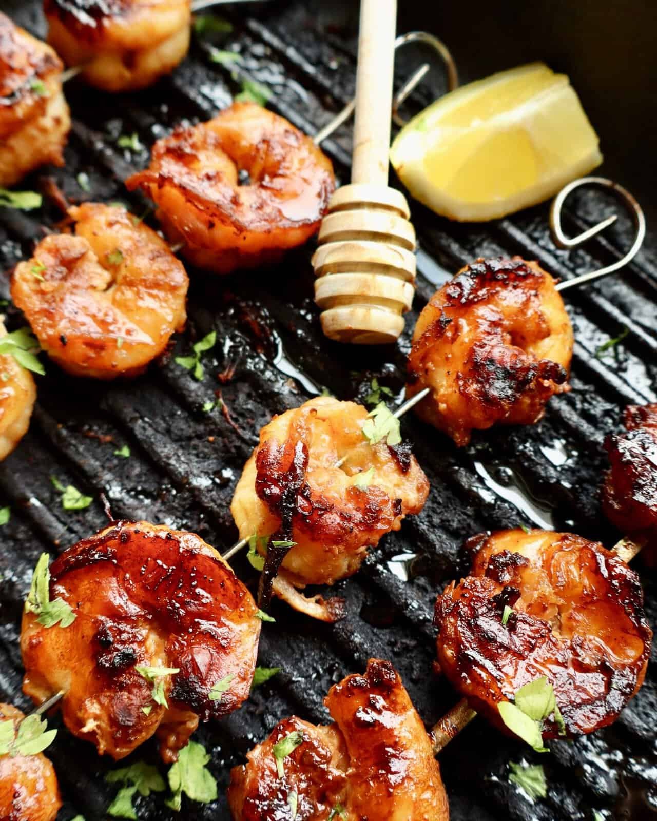 Grilled honey garlic shrimp skewers with fresh herbs and lemon wedge on a black grill. Made with this honey garlic shrimp marinade.
