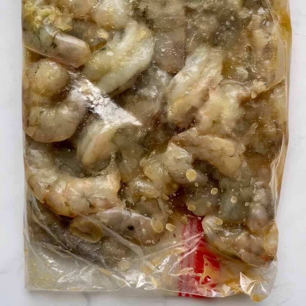 Raw shrimp marinating in honey garlic marinade in a plastic bag.