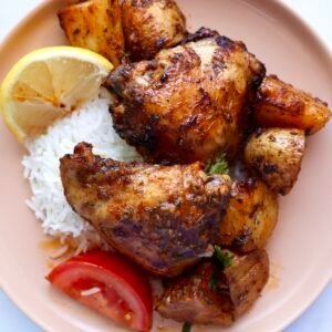 Juicy paprika chicken marinade served with rice, lemon, and tomato on a pink plate.