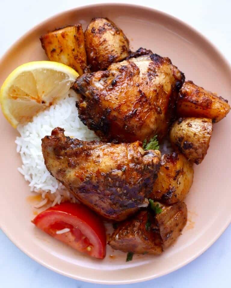 Juicy paprika chicken marinade served with rice, lemon, and tomato on a pink plate.