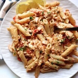 Creamy salmon feta pasta bake with lemon wedges on a white plate.
