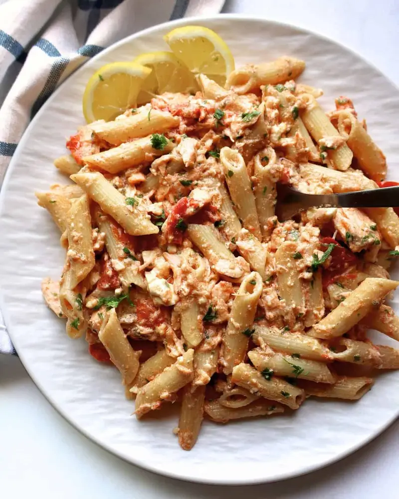 Creamy salmon feta pasta bake with lemon wedges on a white plate.