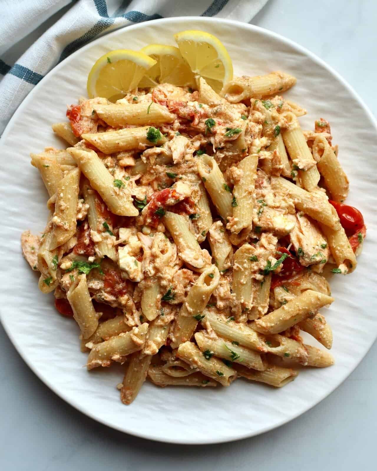Creamy salmon feta pasta bake with lemon wedges on a white plate.