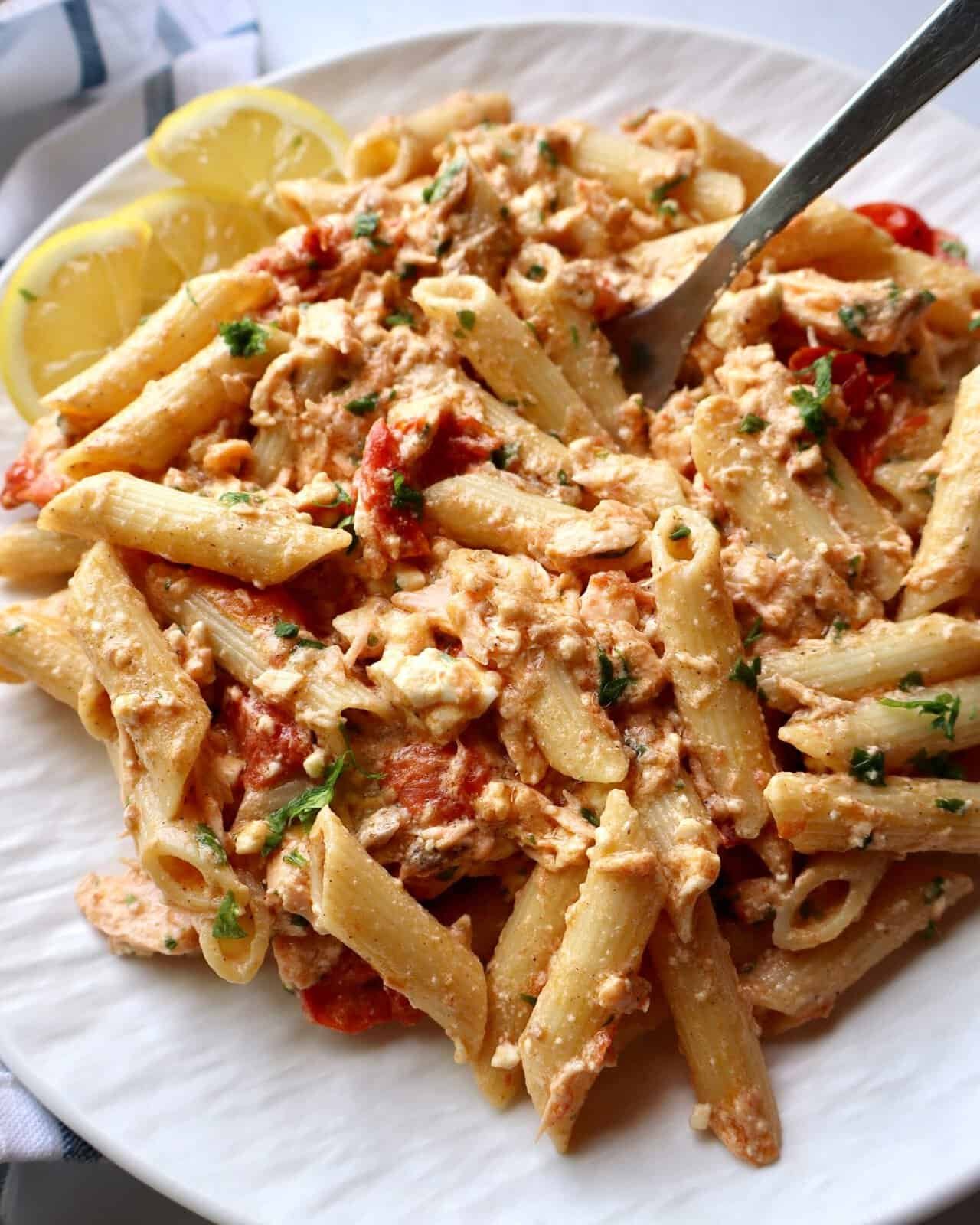 Creamy salmon feta pasta bake with fresh herbs and lemon wedges for a delicious one-pan dinner. Perf.
