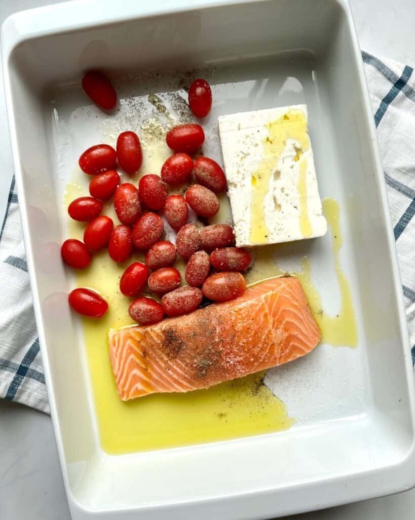 Creamy salmon, cherry tomatoes, feta cheese, and olive oil in a baking dish for a pasta bake.