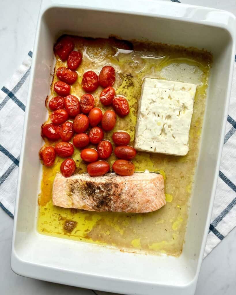 Creamy salmon, cherry tomatoes, and feta cheese baking in a white dish for easy dinner.