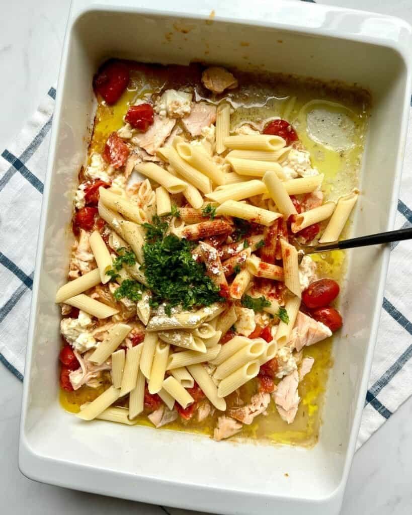 Creamy salmon feta pasta bake in a white baking dish with cherry tomatoes and herbs.