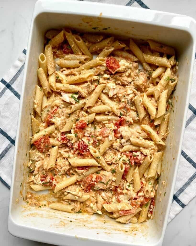 Creamy salmon feta pasta bake in a white casserole dish with pasta, salmon, feta cheese, and tomatoe.