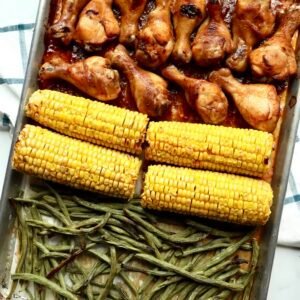 Juicy BBQ chicken drumsticks with roasted corn and green beans on a sheet pan. Perfect easy dinner r.