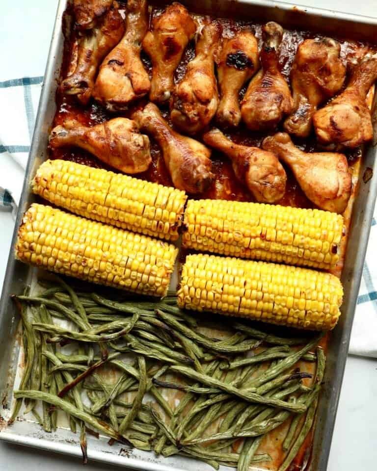 Juicy BBQ chicken drumsticks with roasted corn and green beans on a sheet pan. Perfect easy dinner r.