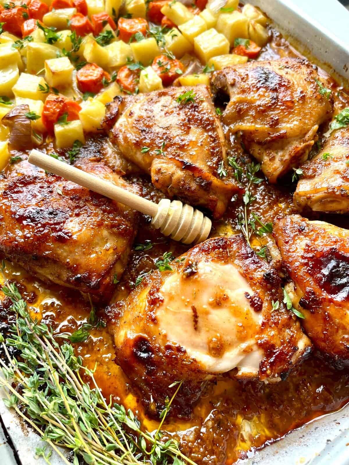 Juicy honey Dijon chicken thighs with roasted vegetables and fresh herbs in a baking dish.