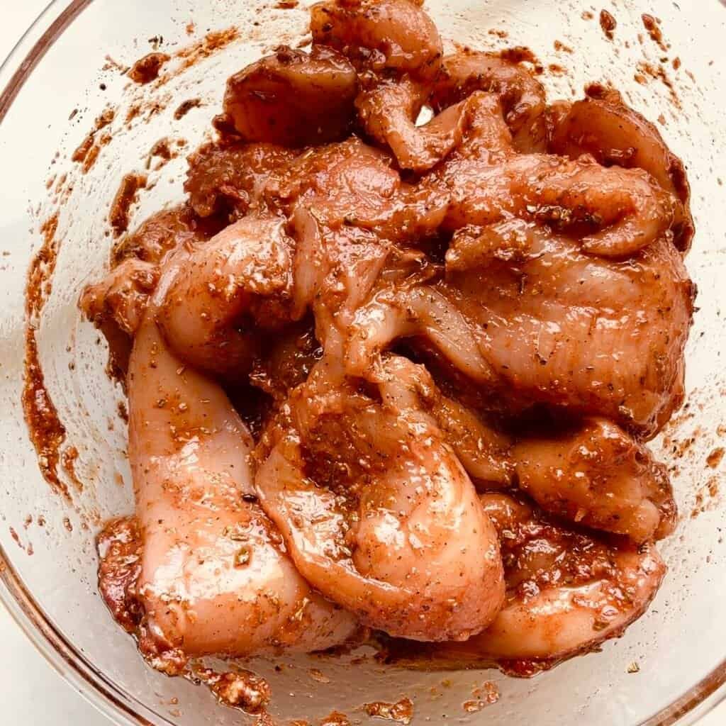 Marinated chicken pieces with tomato herb sauce in a glass bowl.
