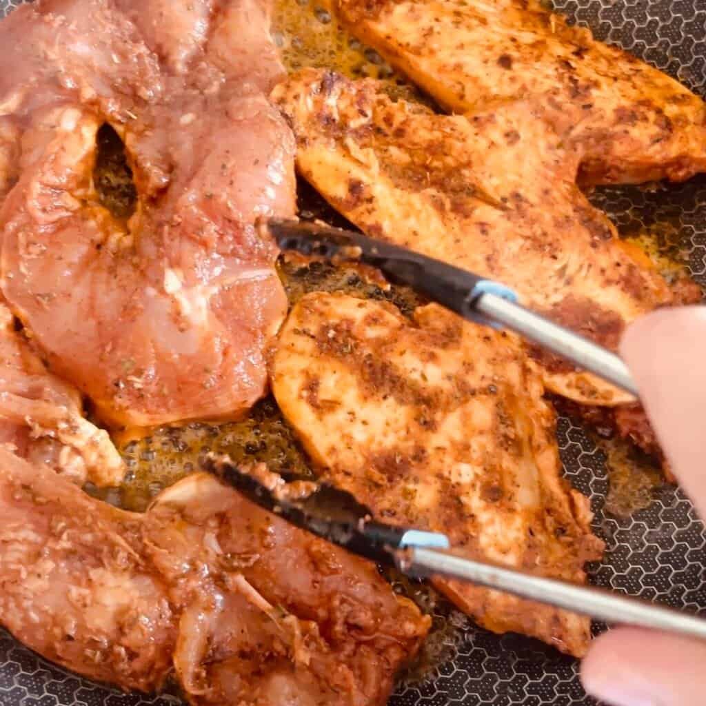 Tomato herb marinated chicken cooking in a skillet.