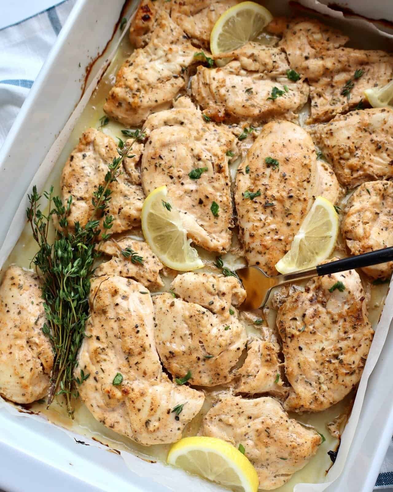 Grilled lemon herb chicken breasts baked in a creamy sauce with fresh herbs and lemon slices.