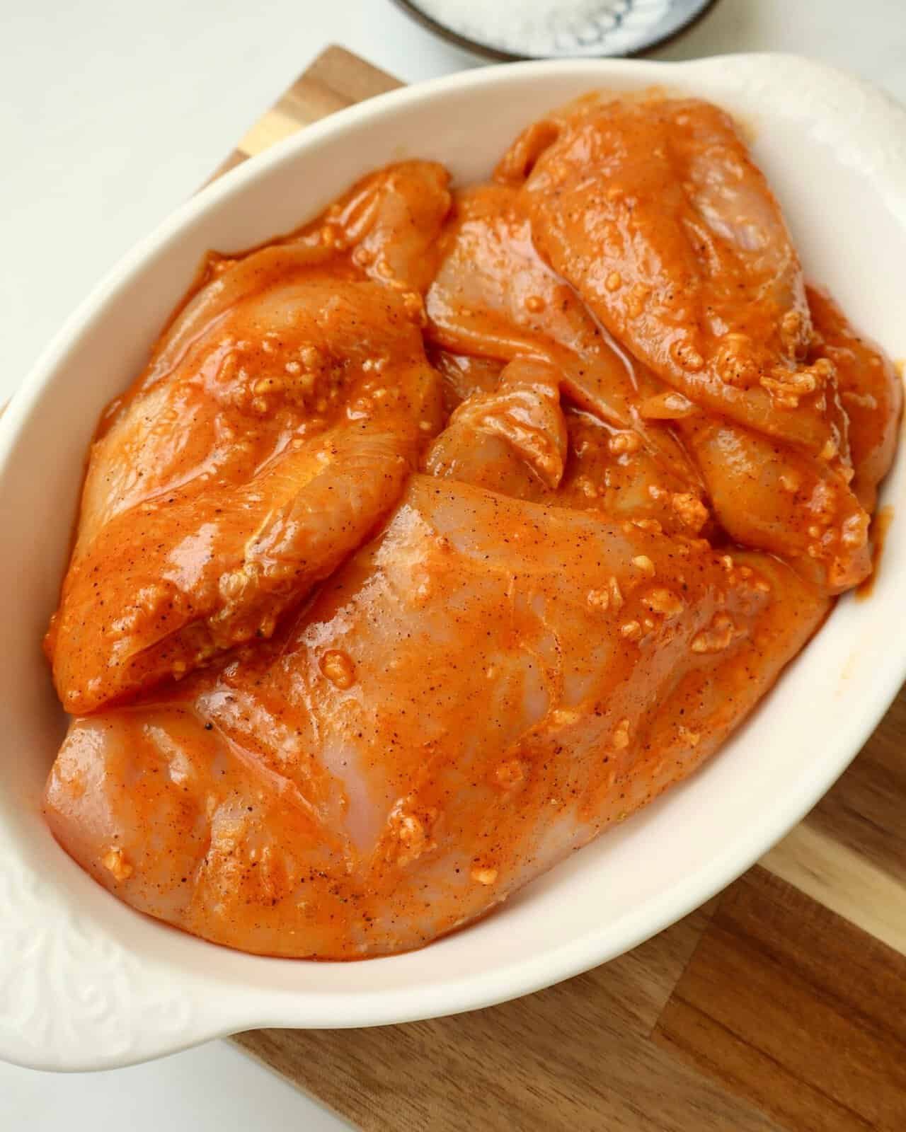 Raw chicken marinade for air fryer in a white bowl with herbs and seasoning