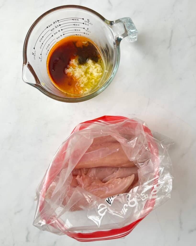 Chicken marinade ingredients in a measuring cup beside raw chicken in a bag