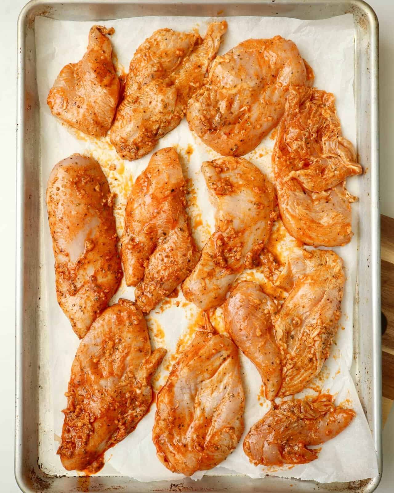 Marinated chicken arranged on a baking sheet before baking in the oven