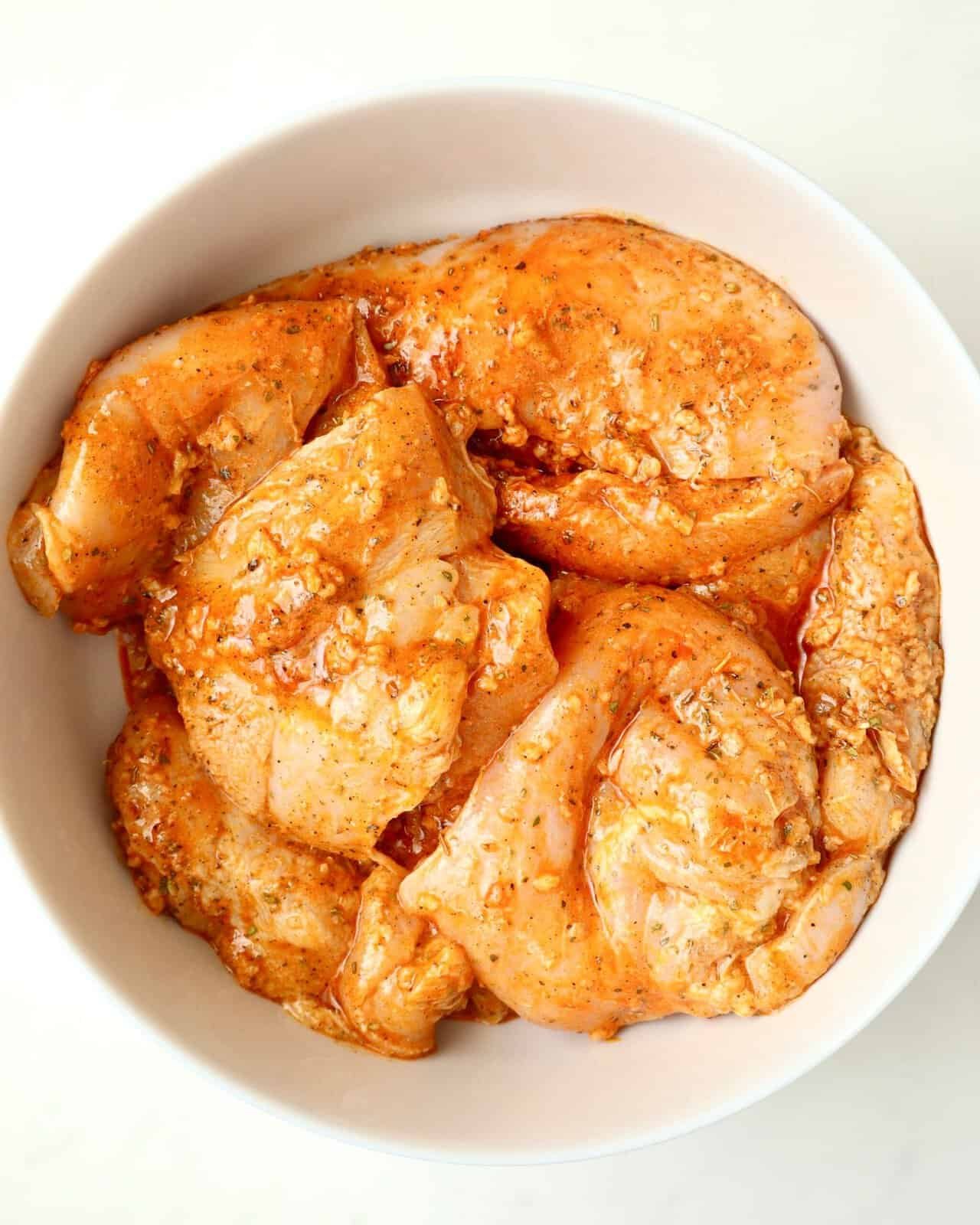 Chicken breasts marinating in a bowl with garlic, oil, and spices