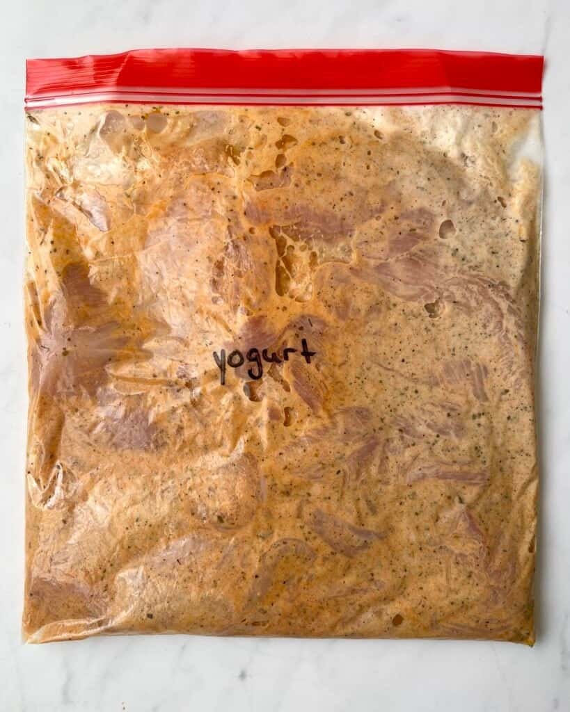 Raw chicken coated in garlic yogurt marinade in a sealed zip lock bag