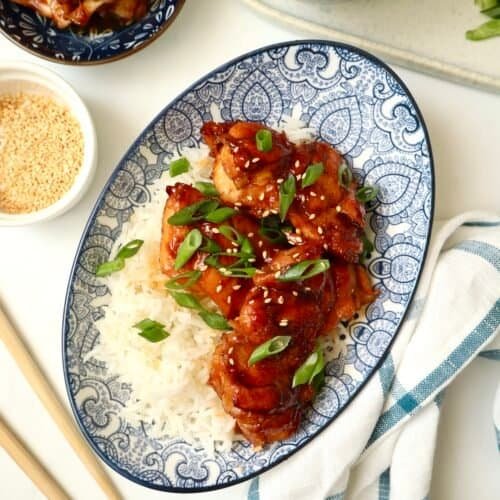 Sticky gochujang chicken thighs served over rice with green onions and sesame seeds.