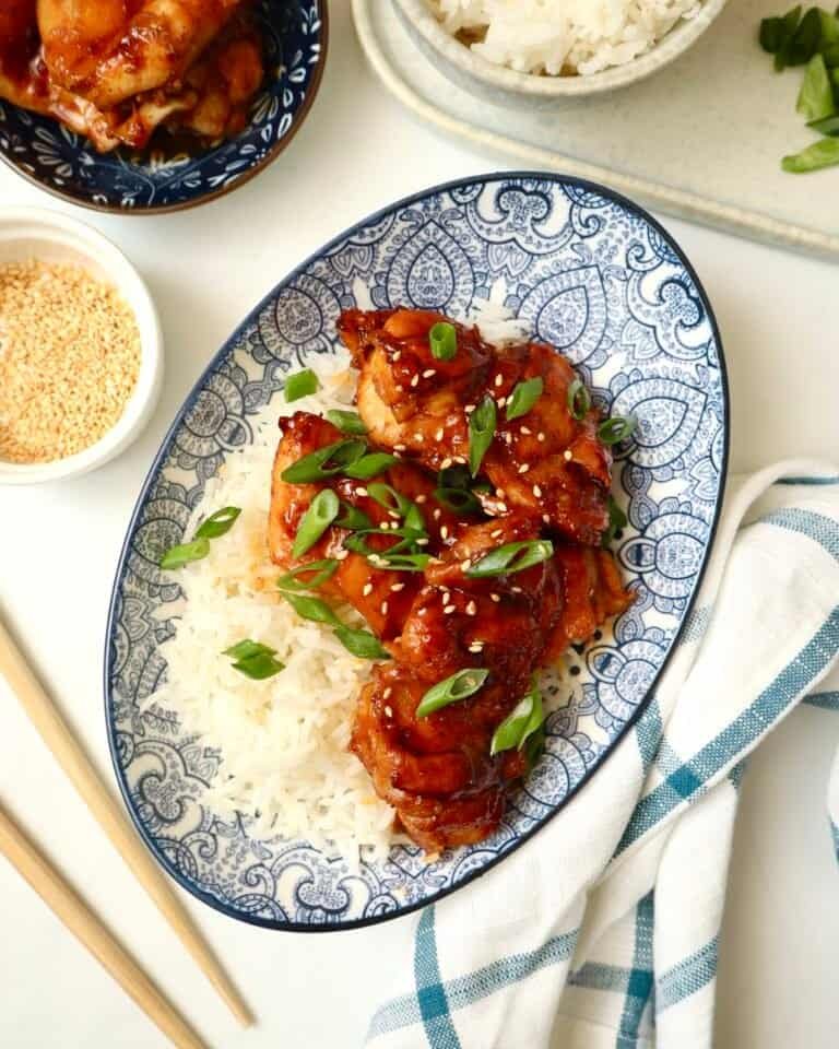 Sticky gochujang chicken thighs served over rice with green onions and sesame seeds.
