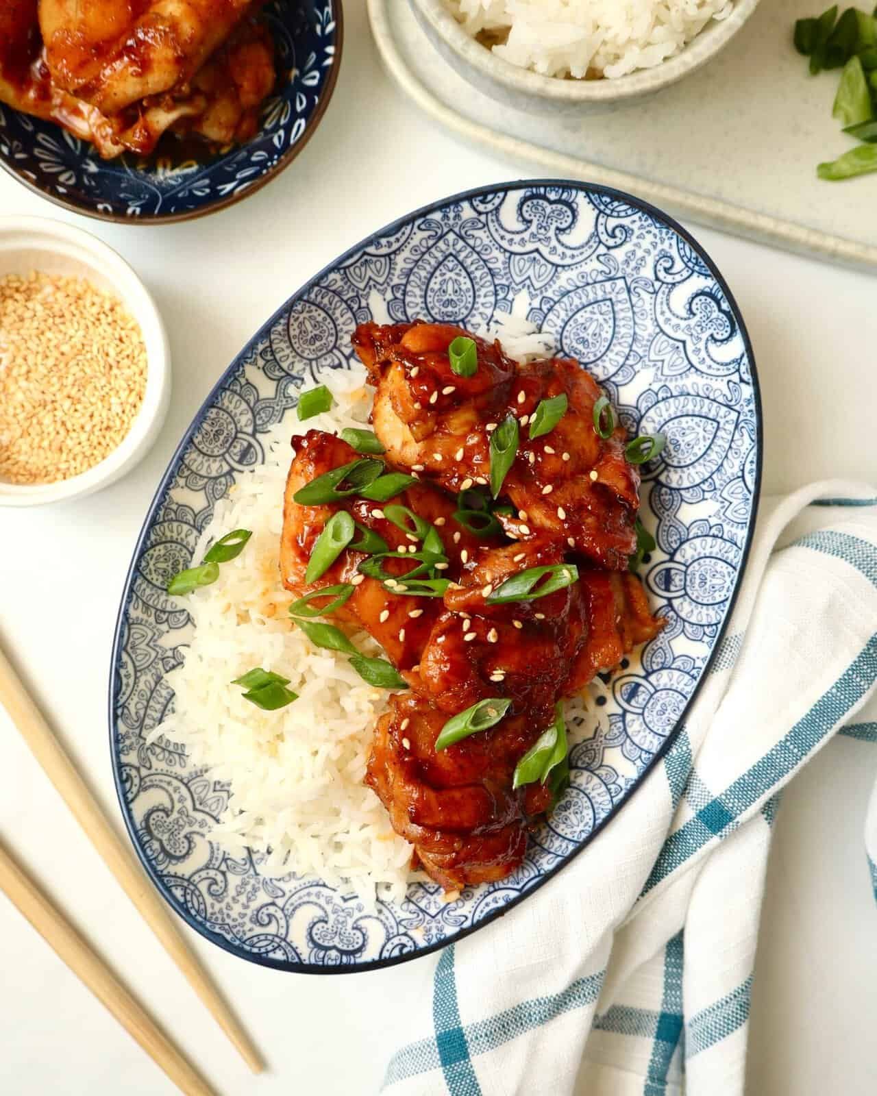 Sticky gochujang chicken thighs over rice topped with sesame seeds and green onions.