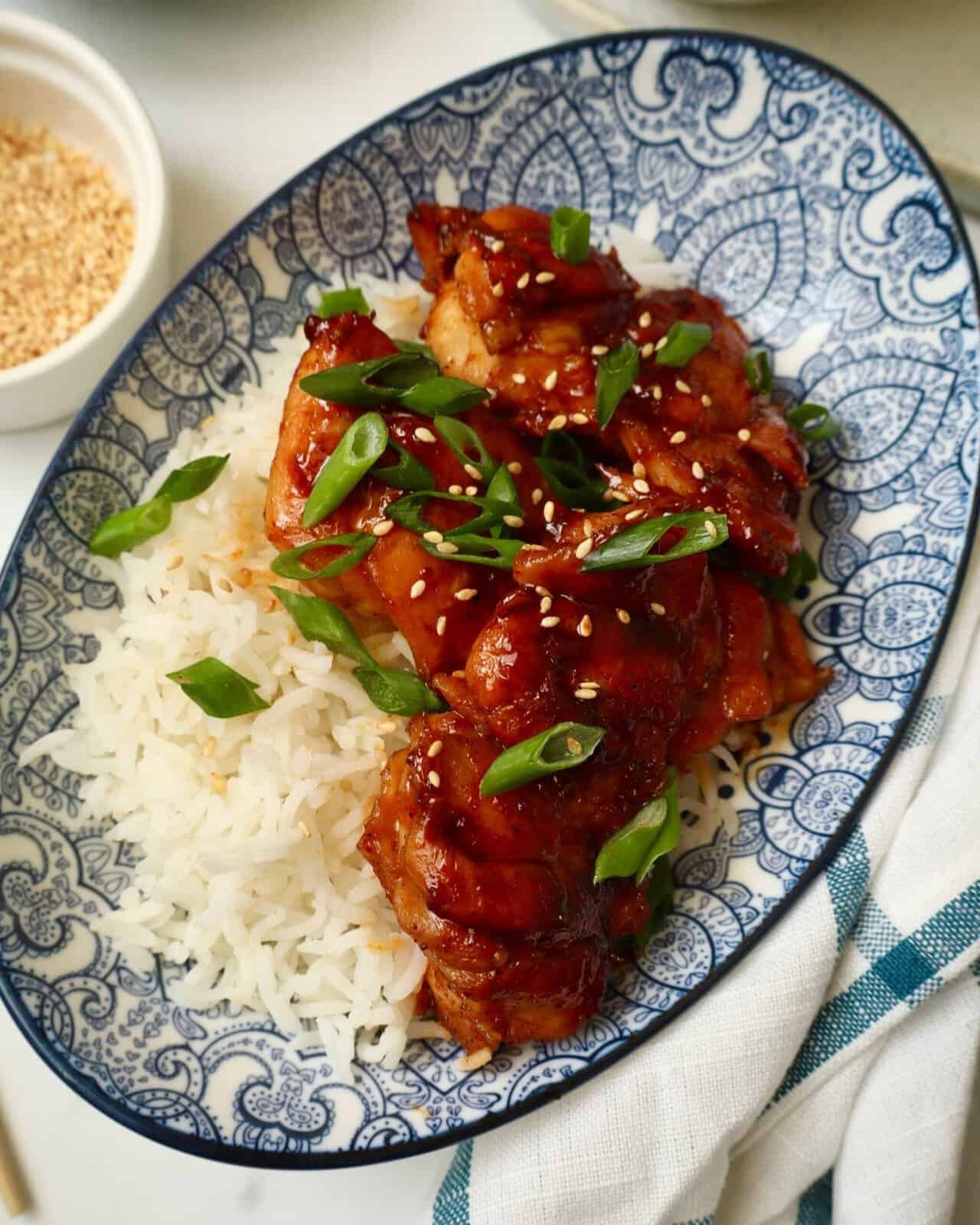 Sweet and spicy Asian chicken with rice, garnished with green onions and sesame seeds.