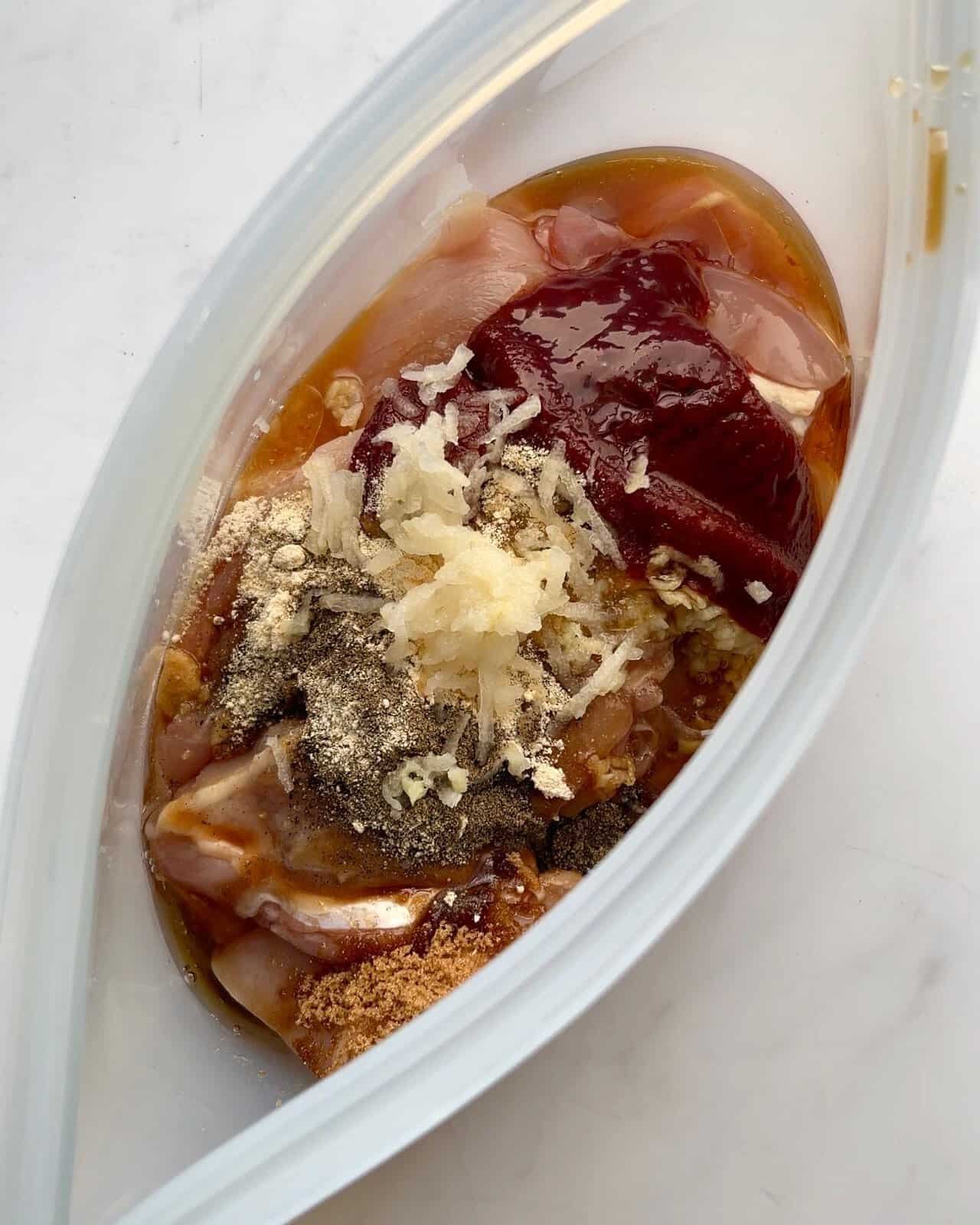 Grilled chicken marinade with soy sauce, garlic, ginger, and spices in a glass container.