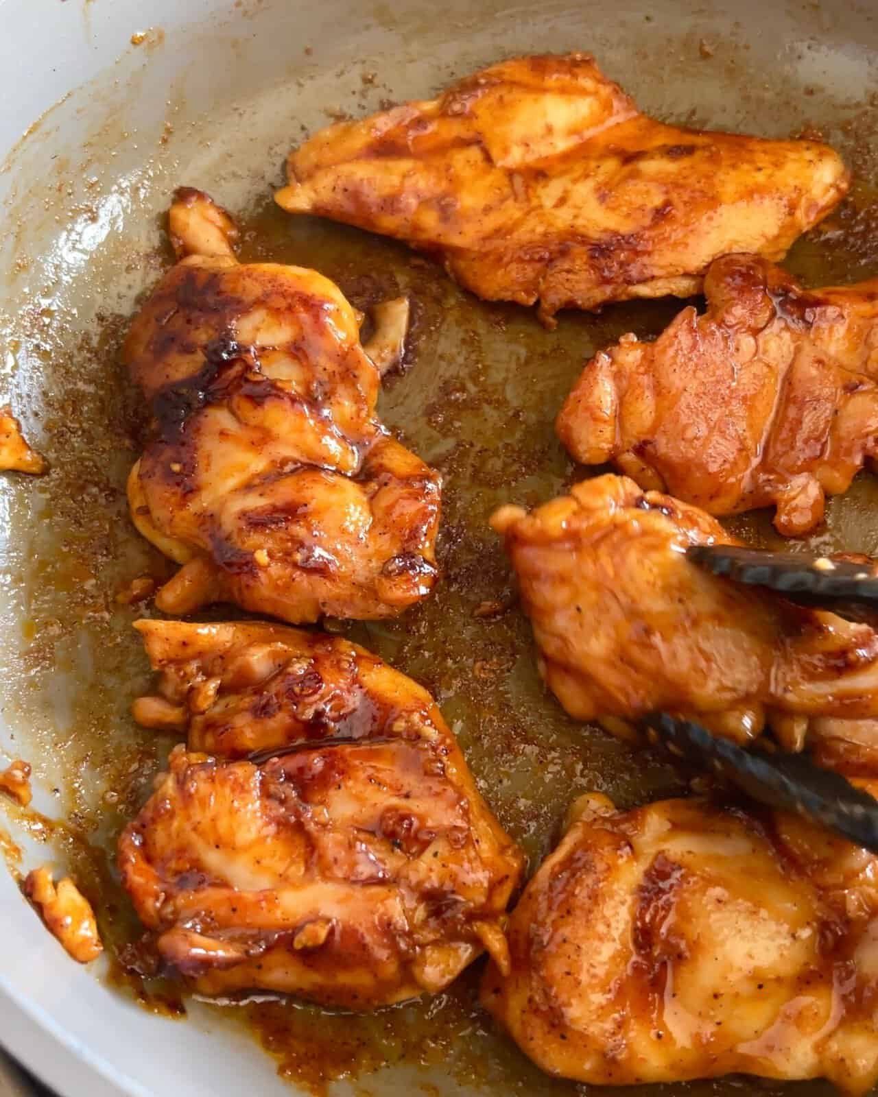 Chicken thighs cooking in a skillet with sticky caramelized gochujang glaze.