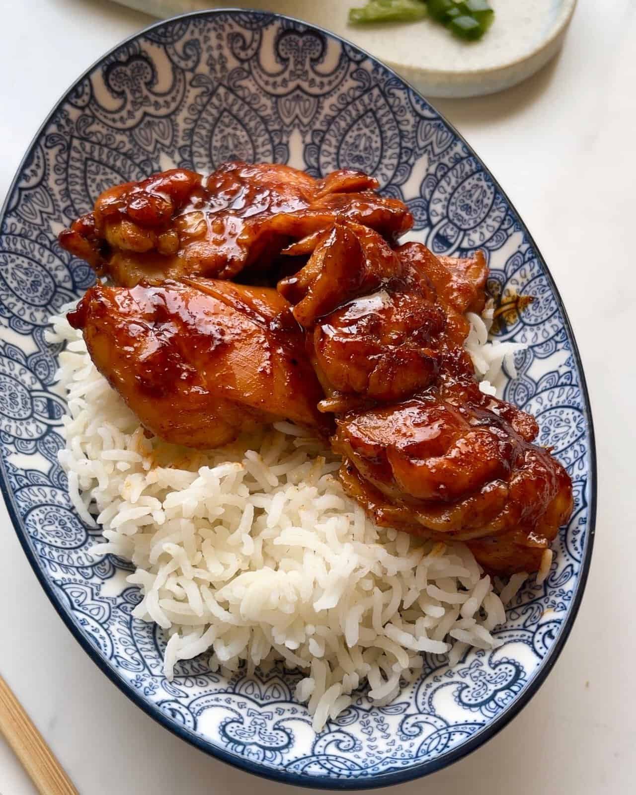 Grilled chicken thighs with savory sauce served over white rice on a decorative blue and white plate.