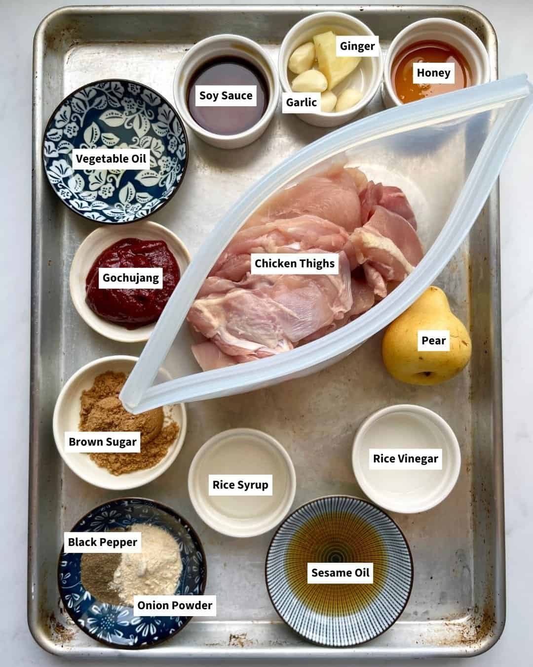 Ingredients for gochujang chicken marinade including Korean chili paste, garlic, soy sauce, ginger, and chicken thighs in small bowls