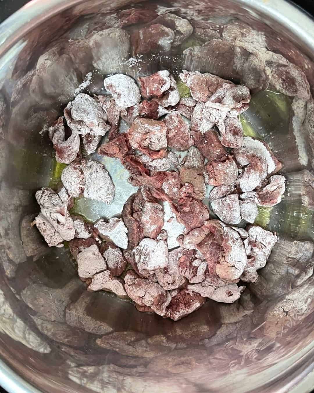 Flank steak coated in cornstarch being added to Instant Pot for browning