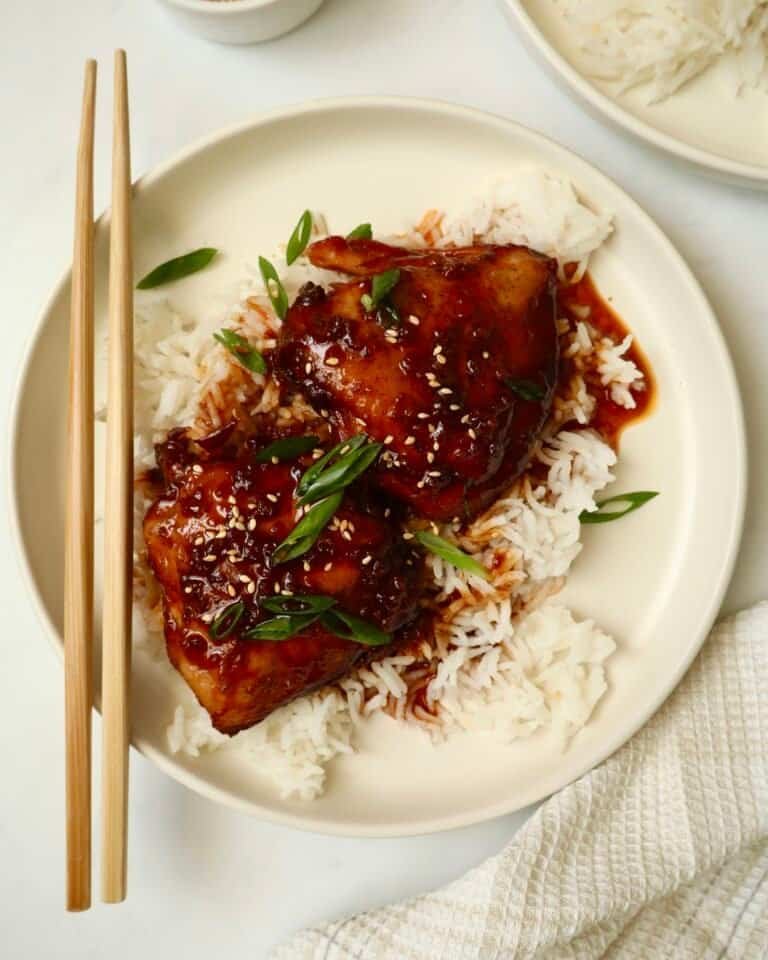 Grilled chicken thighs with spicy Asian sauce served over steamed white rice on a white plate.