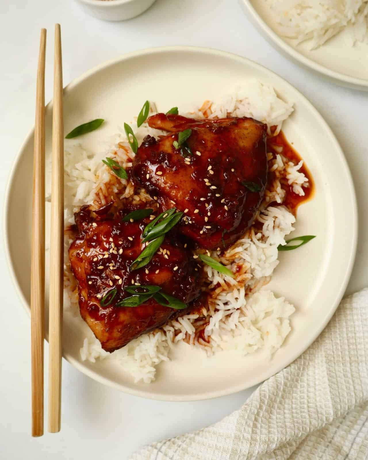 Slow cooker sticky garlic chicken with sauce served over steamed white rice on a white plate.