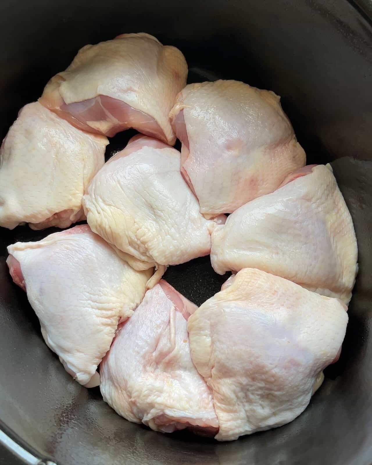 Raw chicken thighs in a slow cooker pot, ready for seasoning and cooking.