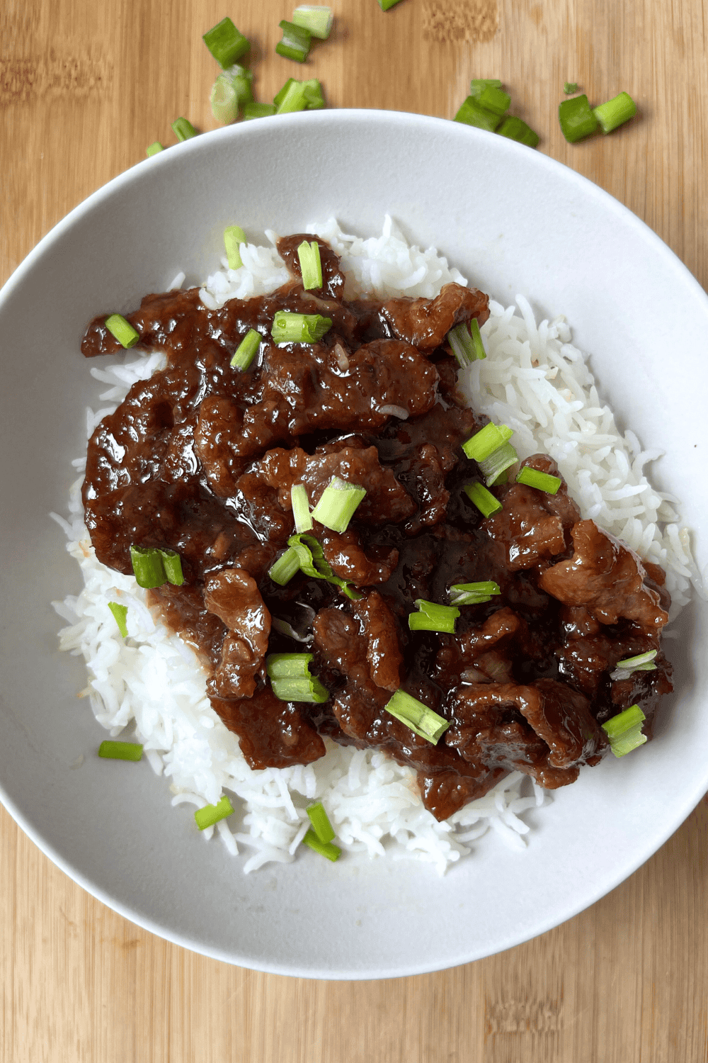 Homemade Mongolian beef in a bowl over rice with shiny caramelized sauce and chopped green onions