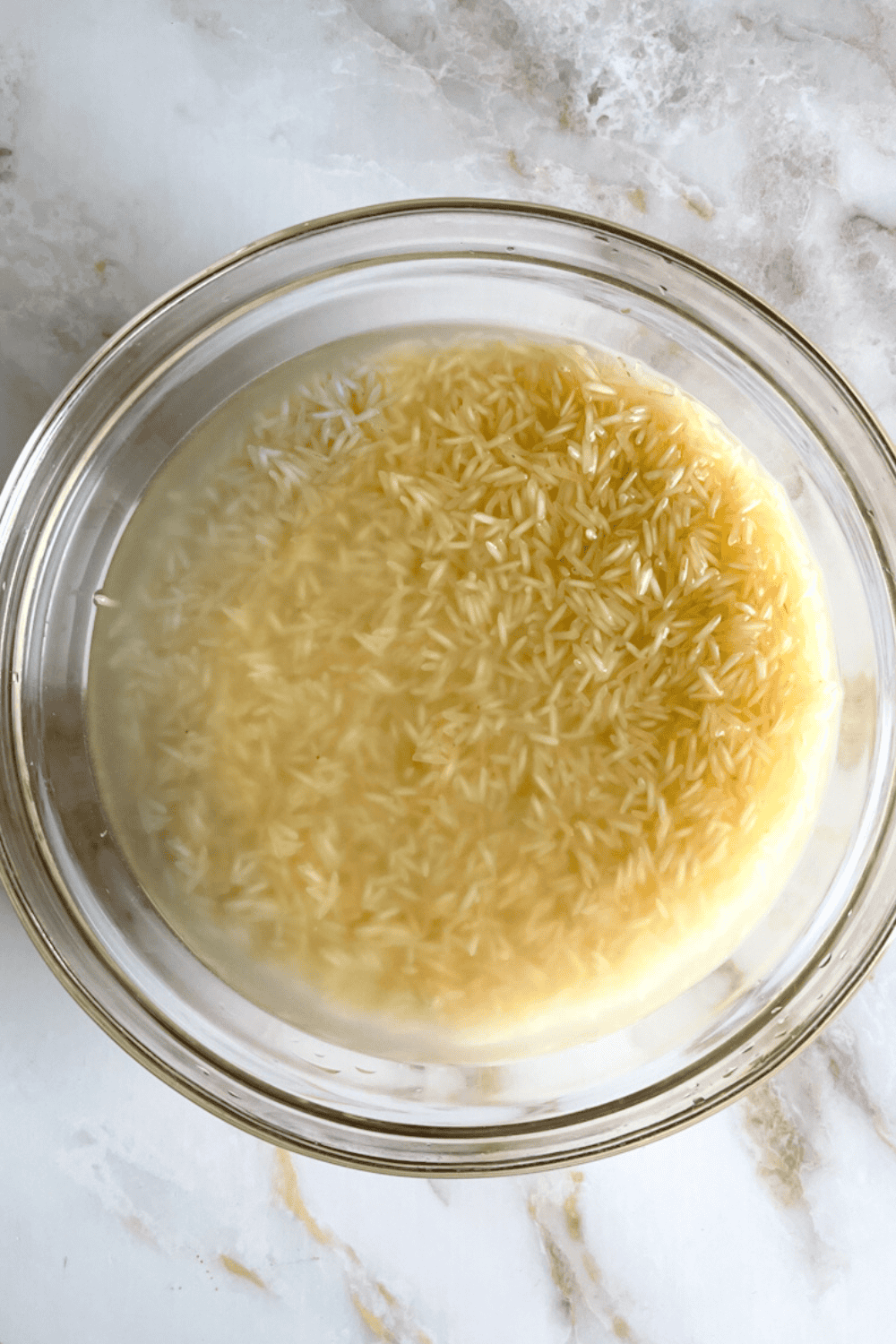 Long grain white rice being rinsed in a bowl with water to remove starch before cooking Lebanese rice with vermicelli