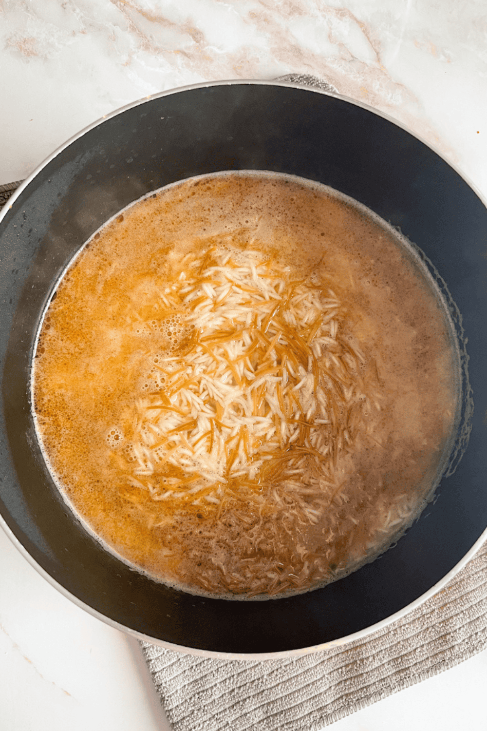 Rice, water, and toasted vermicelli combined in a pot before cooking on the stovetop for Lebanese rice pilaf