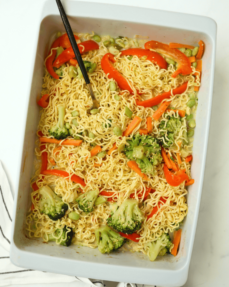Instant ramen noodle stir-fry with broccoli, red bell peppers, and carrots in a white baking dish.