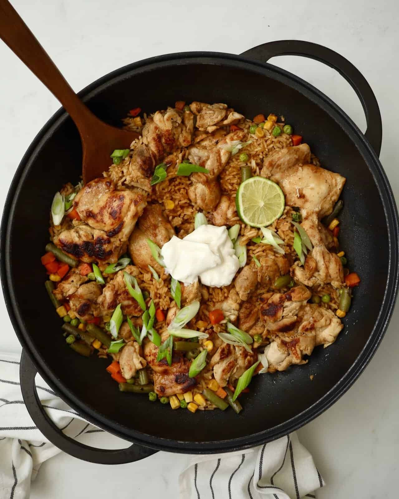 Grilled chicken thighs with vegetables, lime, and sour cream in a black skillet.
