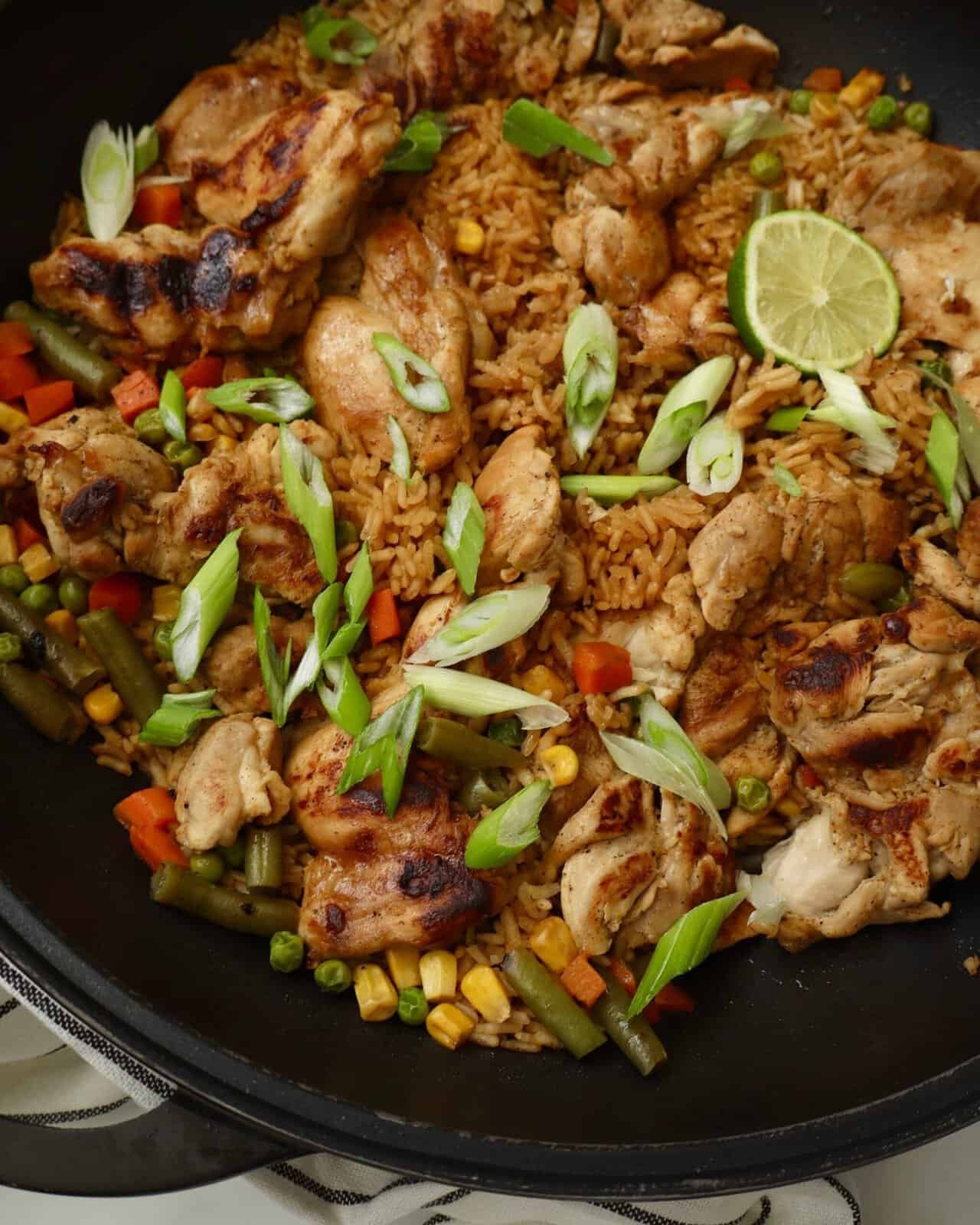 Close up of sticky garlic lime chicken and corn rice skillet with tender chicken thighs, fluffy rice, corn, and green onion garnish